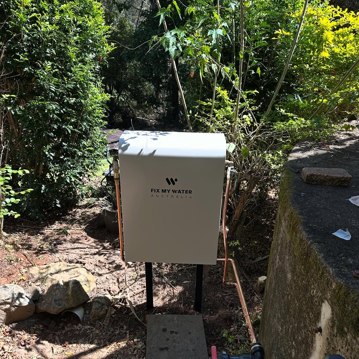 Water filtration unit installed in a white cabinet on a bush block