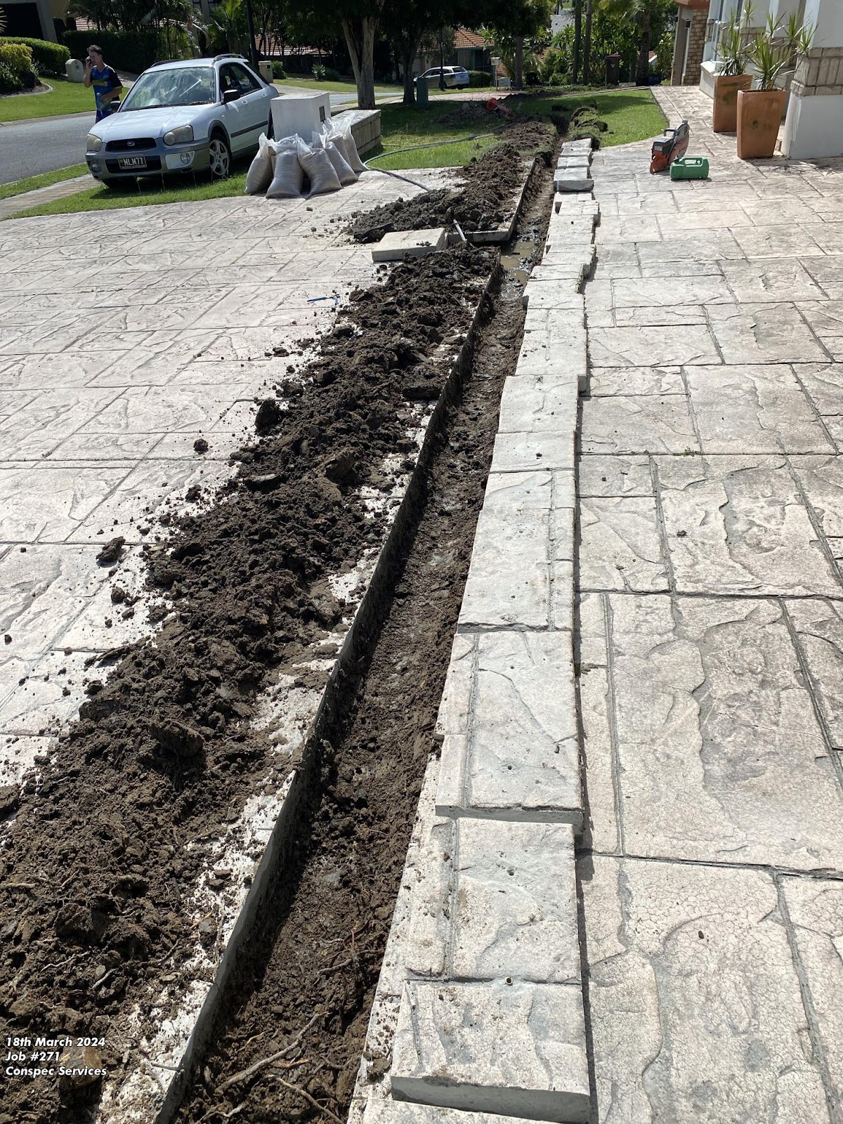 Trench cut through stamped concrete paving with the blocks lifted and stacked to one side